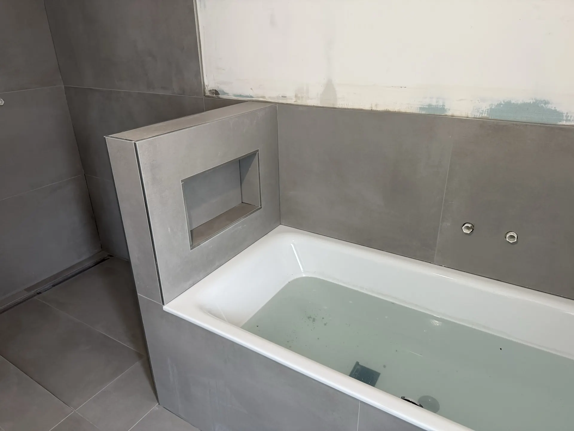 Badewanne mit gefliester Nische und grauen Großformat-Fliesen — EVENT Bau