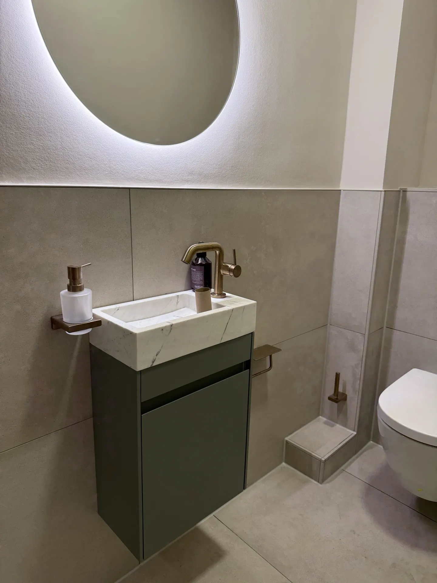 Gäste-WC mit Marmor-Waschtisch, rundem LED-Spiegel und goldenem Wasserhahn